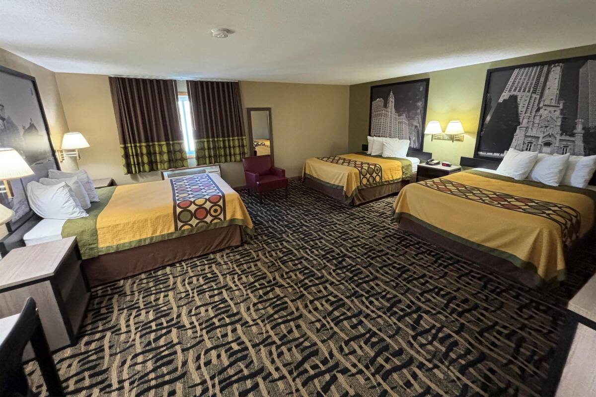 Ein Hotelzimmer mit zwei Betten, einem roten Sessel, einem gemusterten Teppich und zwei Wandleuchten.