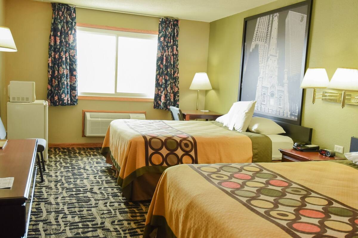 Ein Hotelzimmer mit zwei Betten, einem Schreibtisch, einem Sessel, einer Lampe, einer Uhr und einem gerahmten Bild an der Wand.