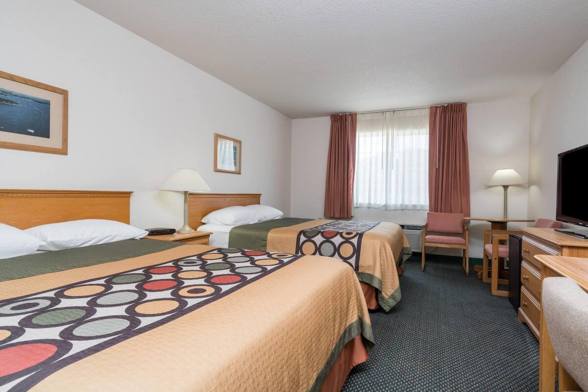A hotel room with two beds, a desk, a chair, a TV, and a window with curtains.