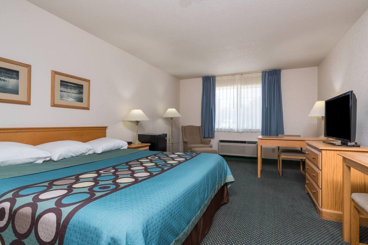 A hotel room with a bed, two bedside lamps, a desk with a television, a chair, and a window with curtains.