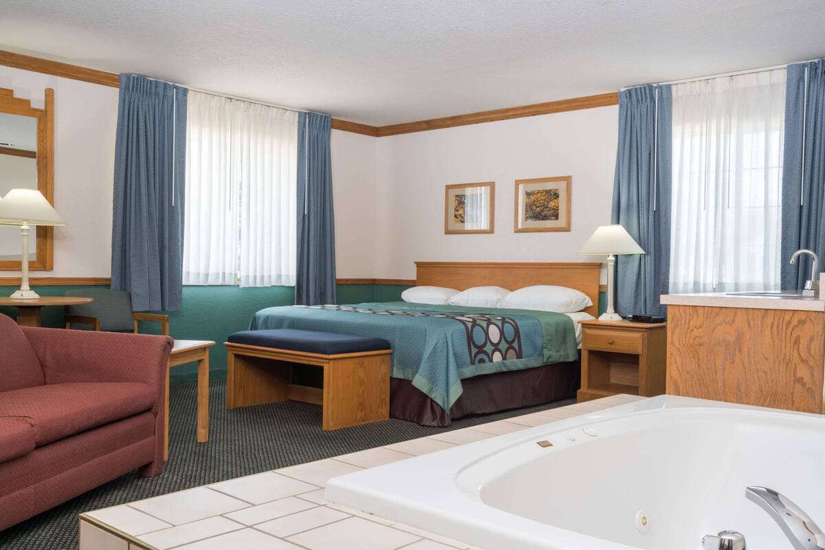 A hotel room with a bed, a desk, a chair, a sofa, a bathroom with a bathtub, and two framed pictures on the wall.