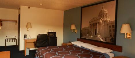 A hotel room with a bed, a desk, a chair, a lamp, and a large framed picture of a building.