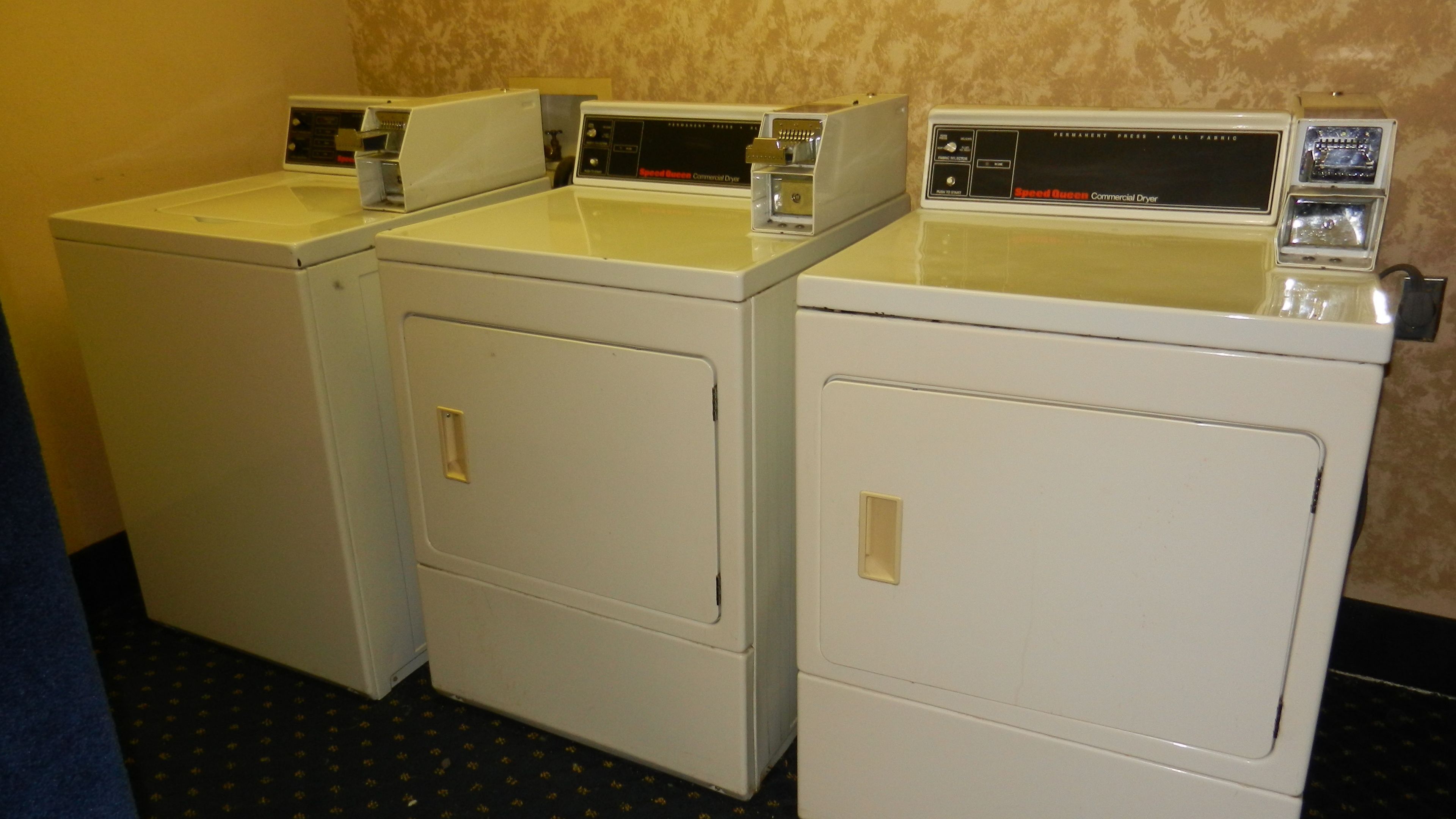 Drie witte wasmachines op een rij in een wasserette.