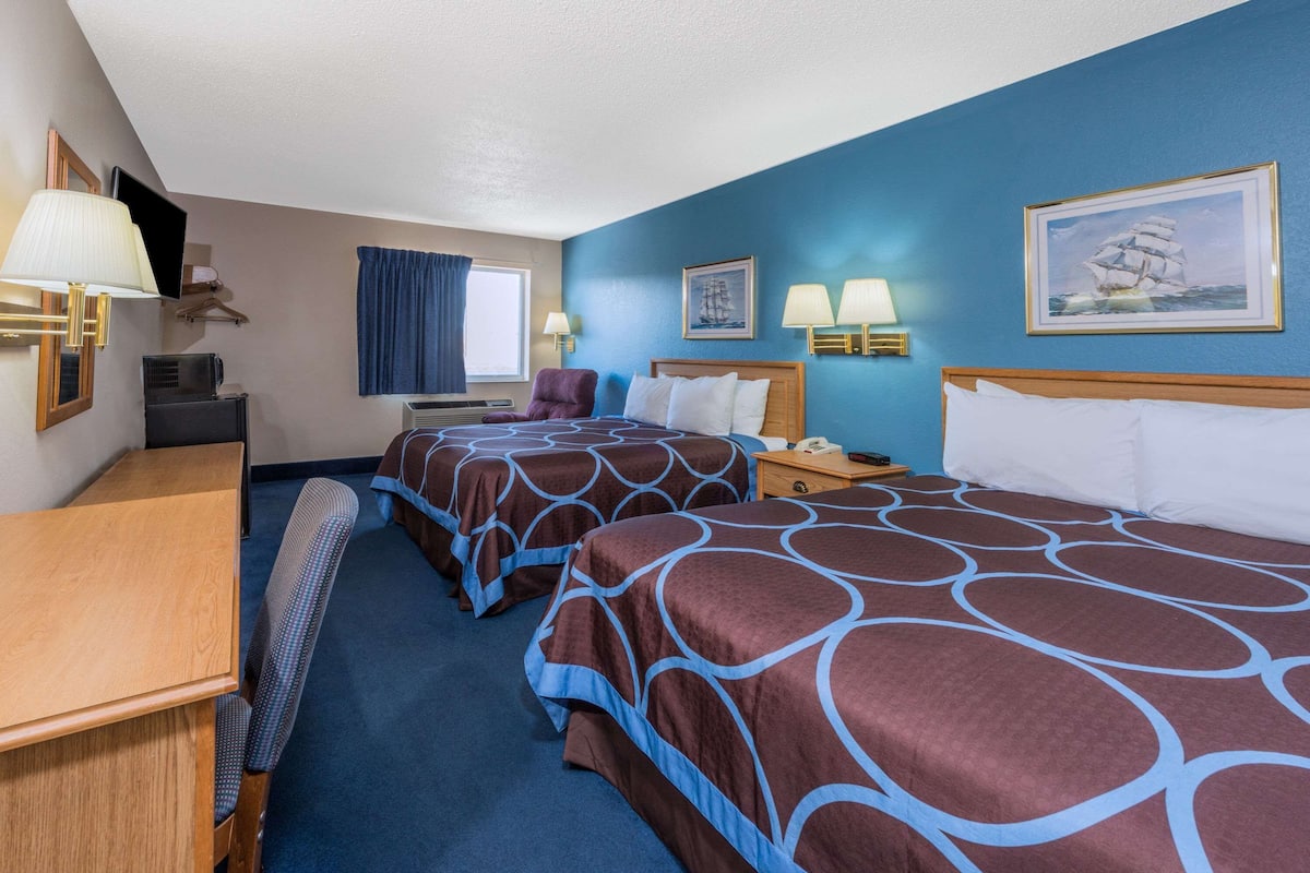 A hotel room with two beds, a desk, a chair, a TV, and a window with curtains.