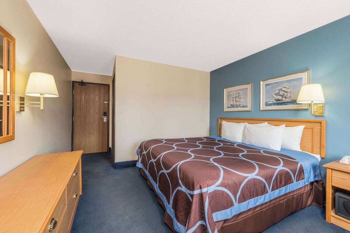 A hotel room with a bed, a wooden dresser, a nightstand, and two wall-mounted lamps.