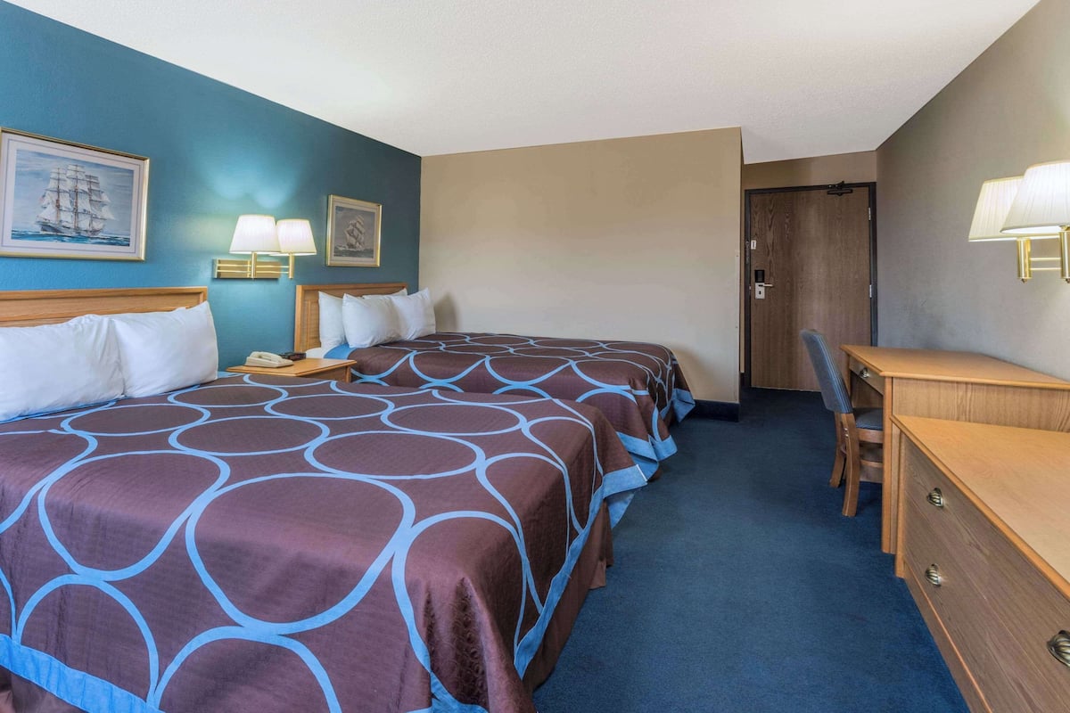 A hotel room with a large bed, a desk, and two wall-mounted lamps.