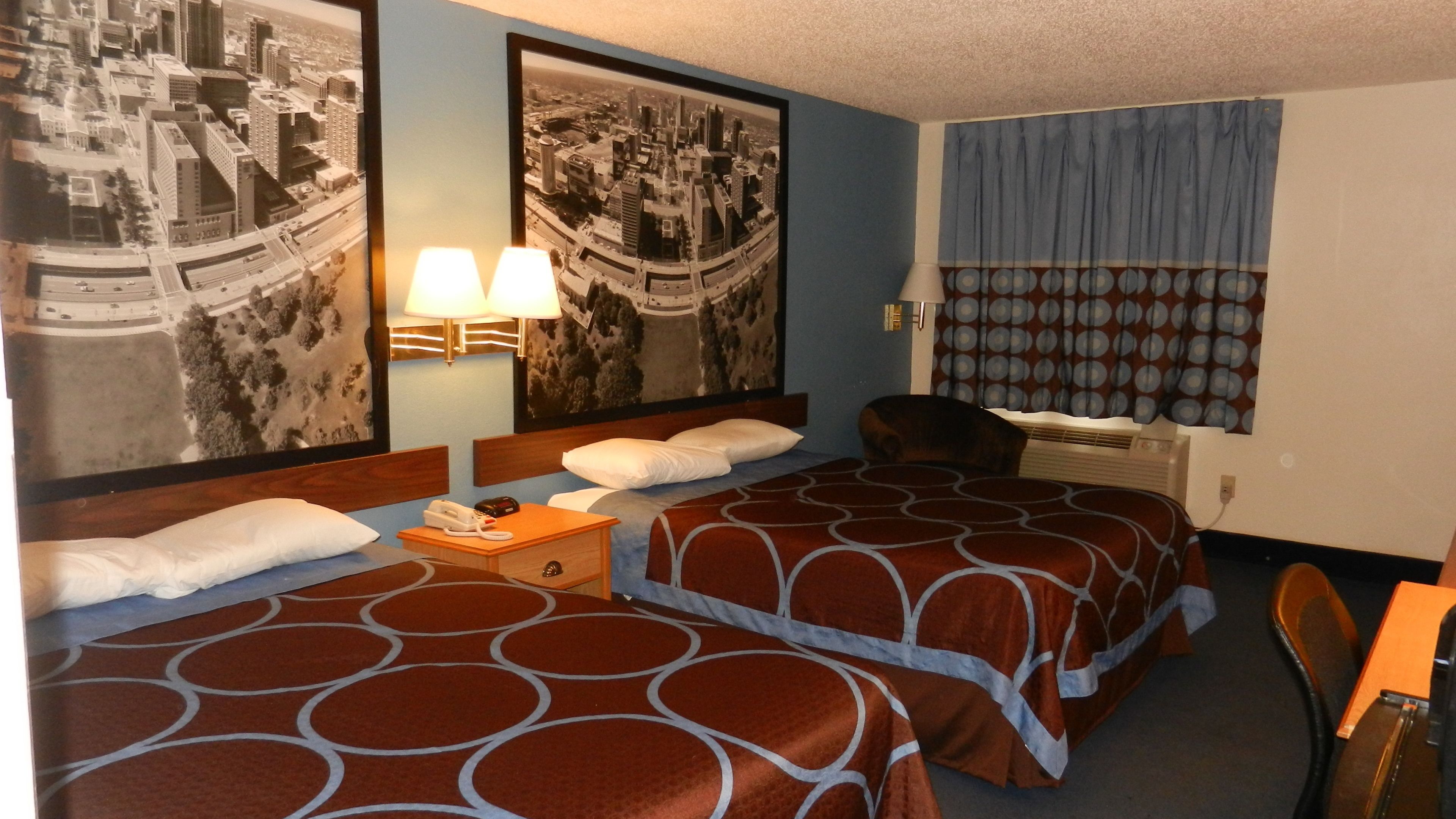 Quarto de hotel com duas camas, uma escrivaninha, uma cadeira, um telefone e duas luminárias de parede.