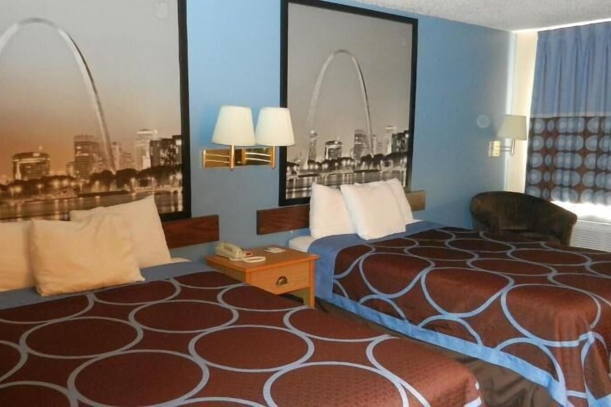 A hotel room with two beds, a nightstand, a lamp, a cityscape mirror, and a window with curtains.