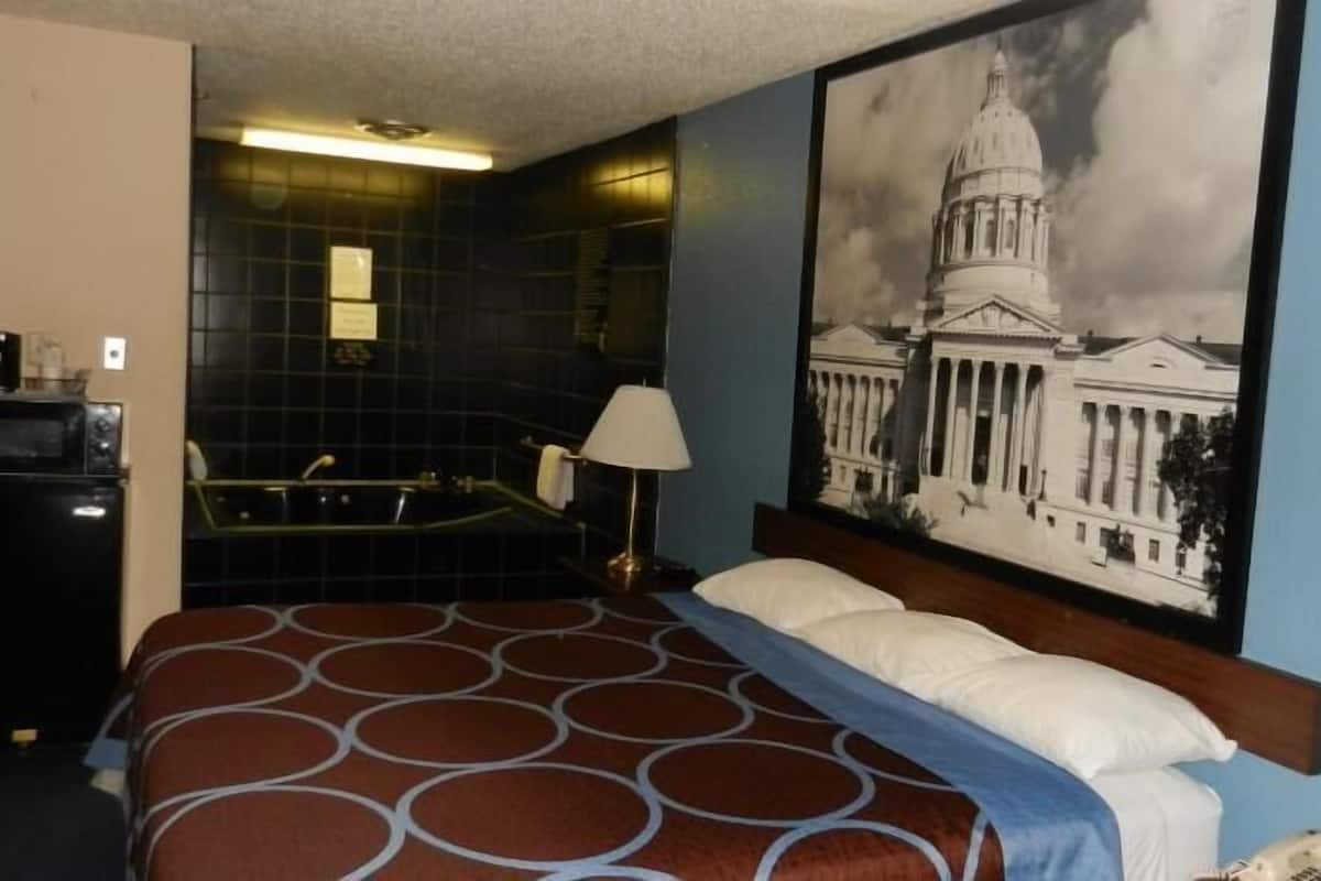A hotel room with a bed, a bathtub, a desk with a computer, and a large wall painting of a building.