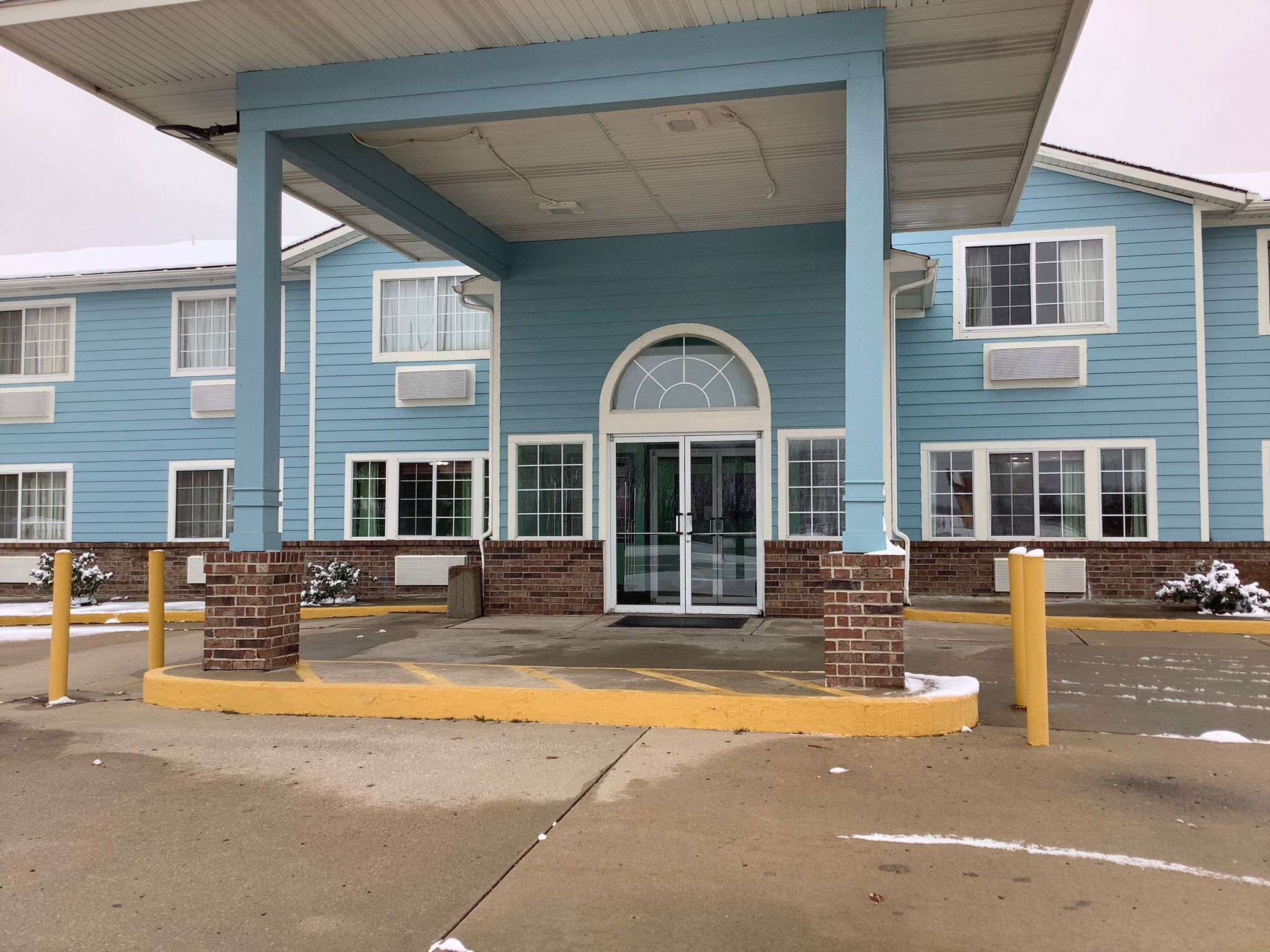 A blue building with a covered entrance, brick pillars, and a yellow curb.