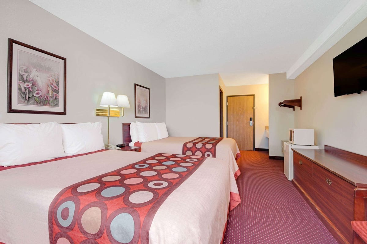 A hotel room with two beds, a desk, a TV, and a door leading to another room.