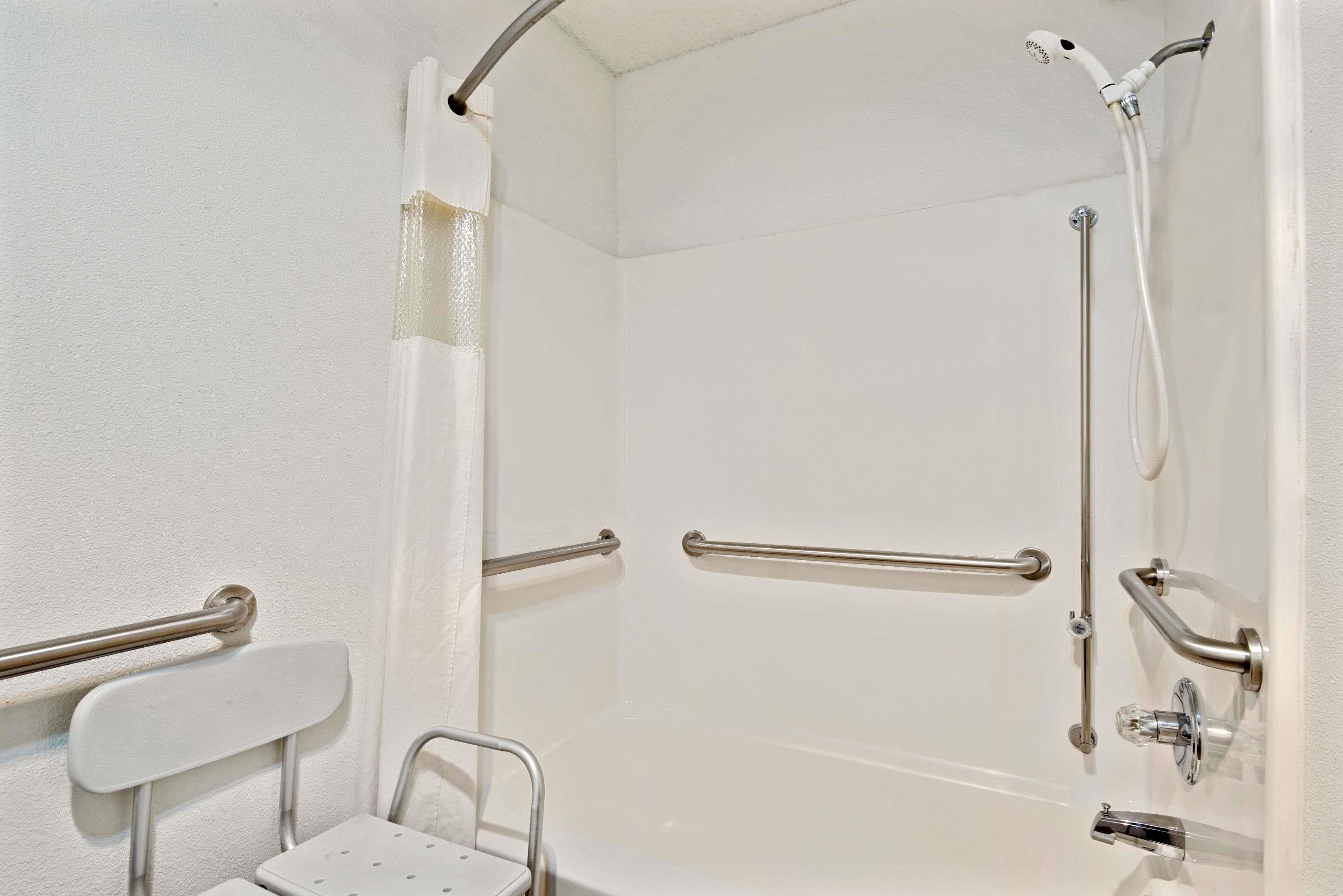 A bathroom with a shower, grab bars, and a wheelchair-accessible bench.