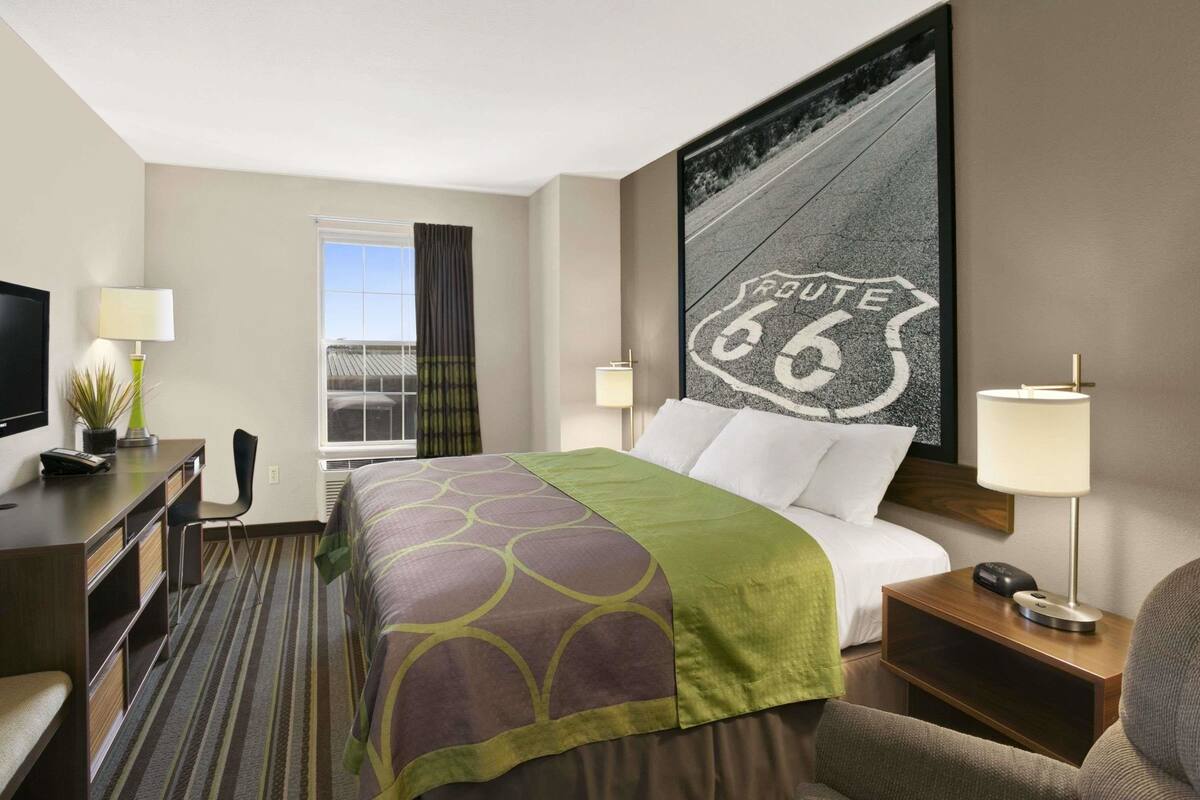 A hotel room with a bed, a desk, a chair, a TV, a window with curtains, and a wall with a Route 66 sign.