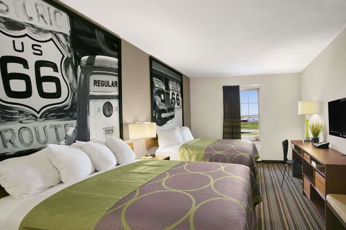 A hotel room with two beds, a desk, a TV, and a window with a view.