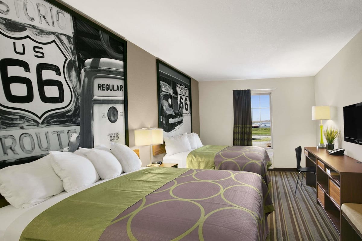 A hotel room with two beds, a television, a desk, and a window with a view.