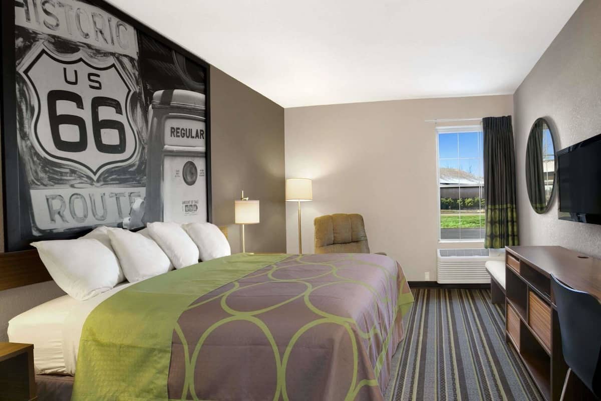A hotel room with a large bed, a desk, a chair, a TV, and a window with a view.