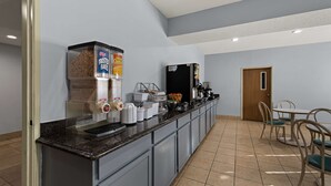 A breakfast bar with cereal, coffee machines, and a refrigerator.