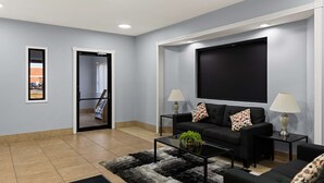 A modern living room with a black sofa set, a coffee table, and a large flat-screen TV mounted on the wall.