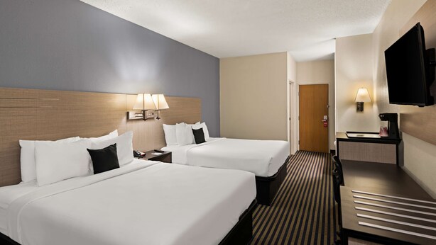 A hotel room with two beds, a desk, a TV, and a lamp.