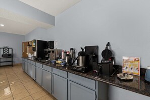 A kitchen with a coffee maker, kettle, and toaster. There is a sign on the counter and a microwave on the left.
