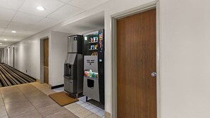 A hotel corridor with a vending machine, a wooden door, and a tiled floor.