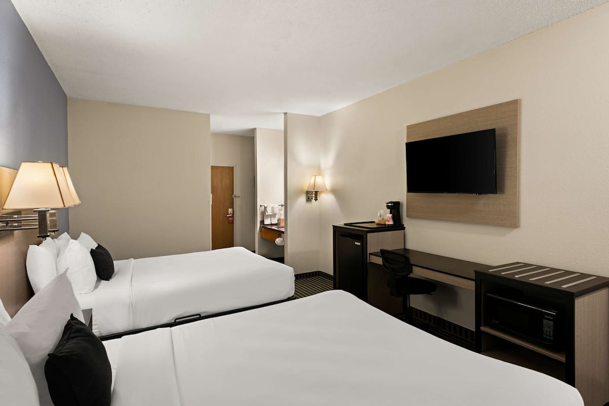 A hotel room with two beds, a desk, a flat-screen TV, a lamp, and a microwave.