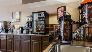 A kitchen area with a coffee station, including a coffee machine, a refrigerator stocked with beverages, and a sink.
