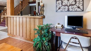 A reception desk with a wooden finish, a computer monitor, a keyboard, and a telephone. There is a potted plant and a bench in the foreground.