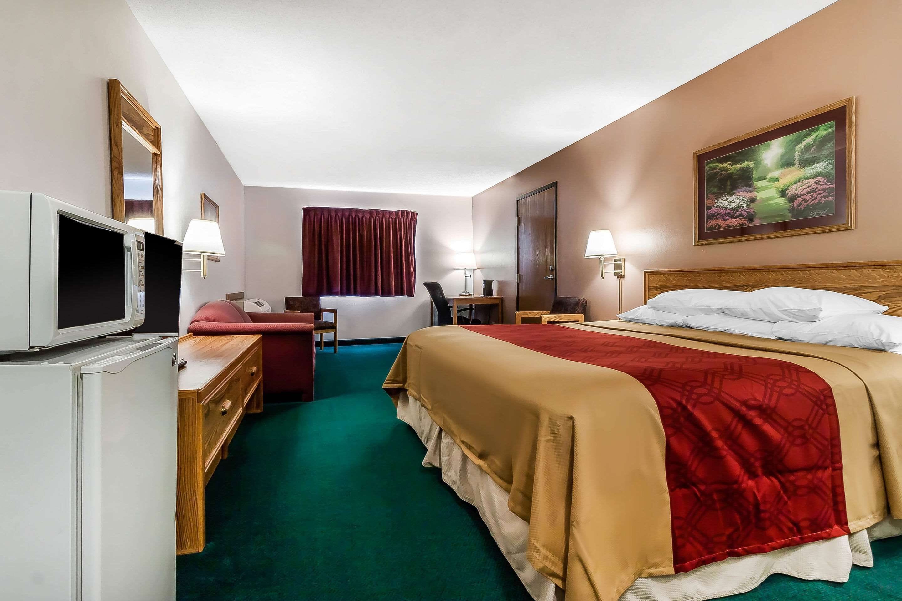 A hotel room with a bed, a desk, a chair, a television, and a painting on the wall.