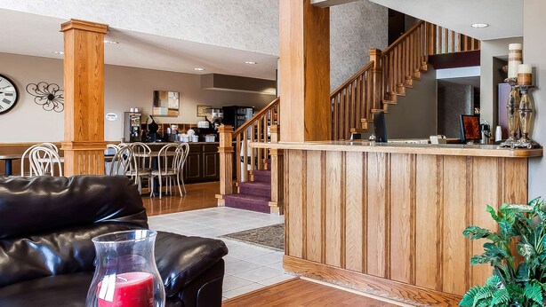 A hotel lobby with a wooden reception desk, a staircase, and a dining area in the background.