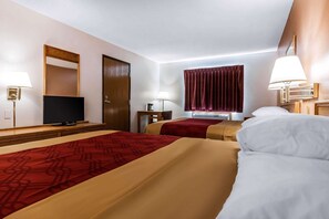 A hotel room with two beds, a television, a desk, and a window with curtains.