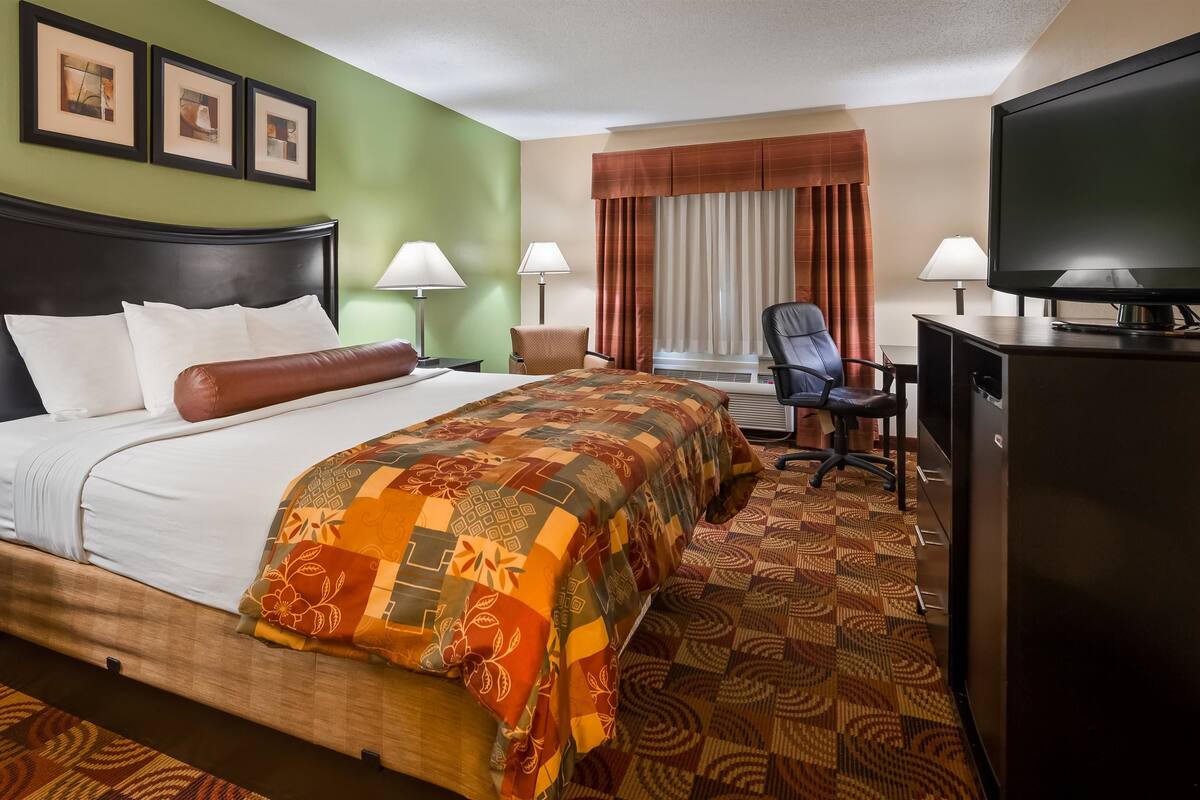 Een hotelkamer met een groot bed, twee bedlampen, een bureau met stoel, een televisie en een raam met gordijnen.