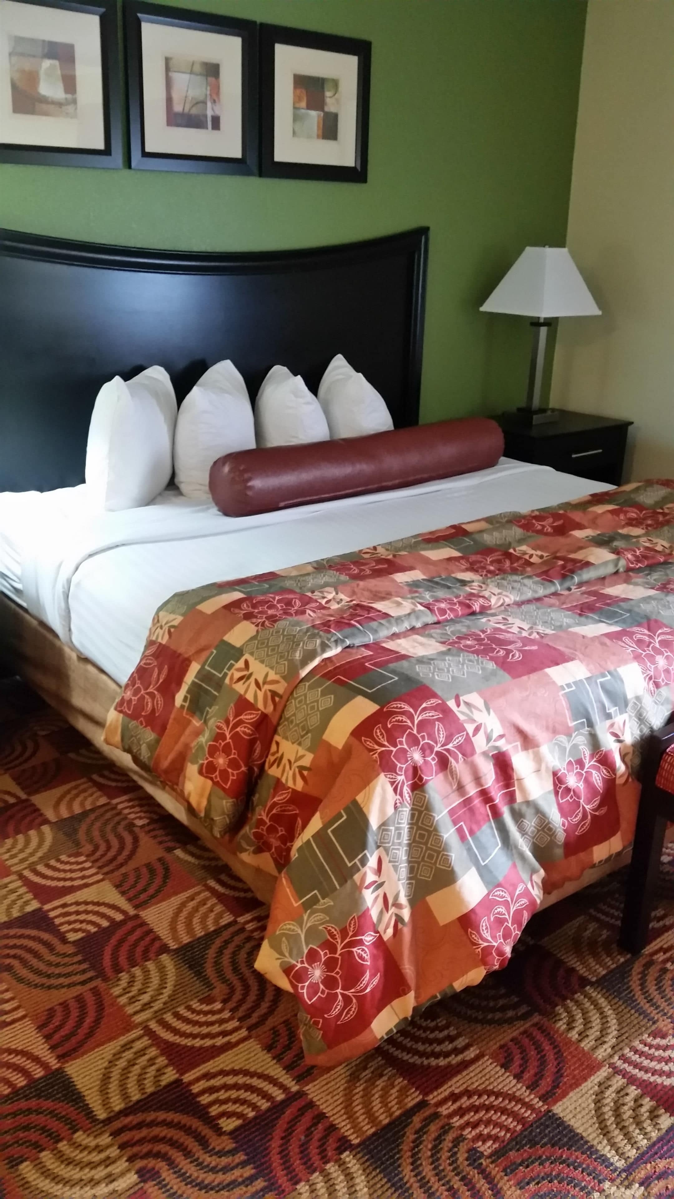 A neatly made bed with a patterned bedspread, a black headboard, and a nightstand with a lamp.