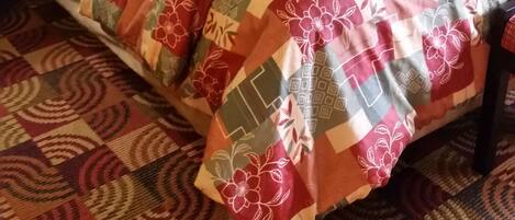 Una cama bien hecha con una colcha estampada, un cabecero negro y una mesita de noche con una lámpara.