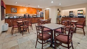 A restaurant with wooden tables and chairs, a kitchen area, and a coffee machine.