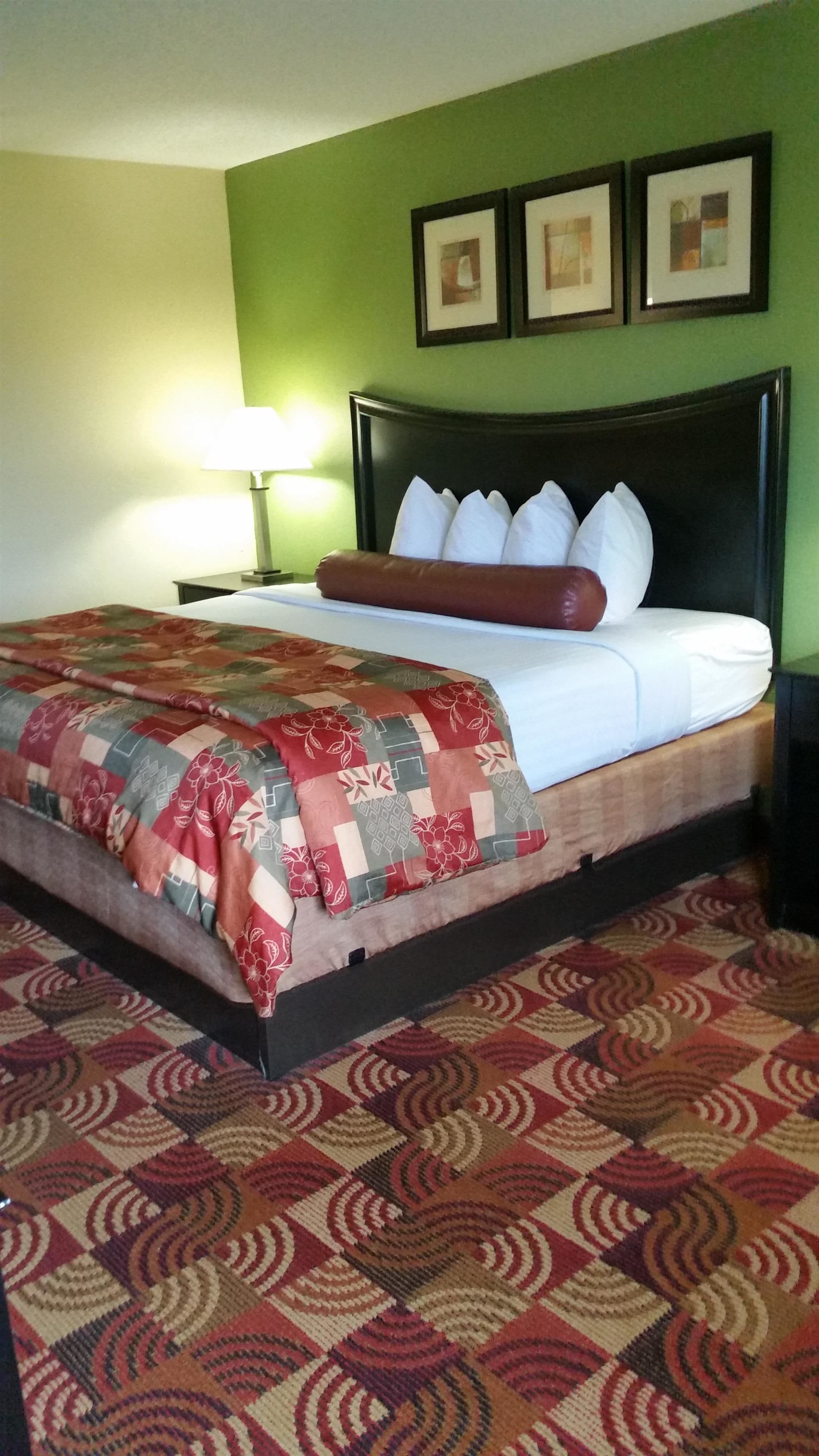 Una cama bien hecha con una colcha de estampado floral, cabecera oscura y pared verde con tres cuadros enmarcados.