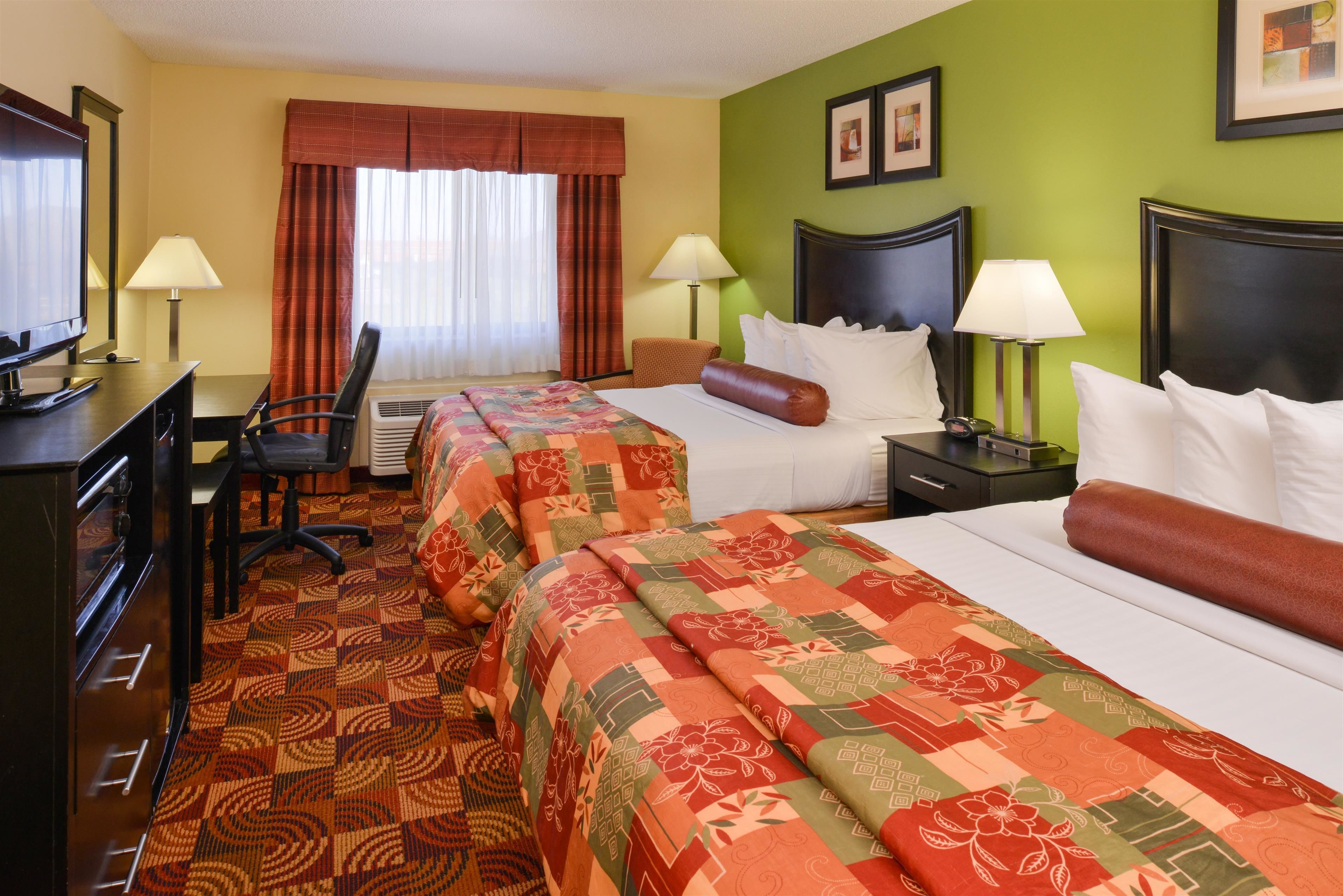 A hotel room with two beds, a desk with a computer, a chair, and a television.