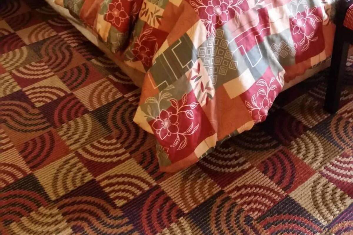 Een bed met een bedsprei met patroon, een zwart hoofdbord, witte kussens en een rood accentkussen.