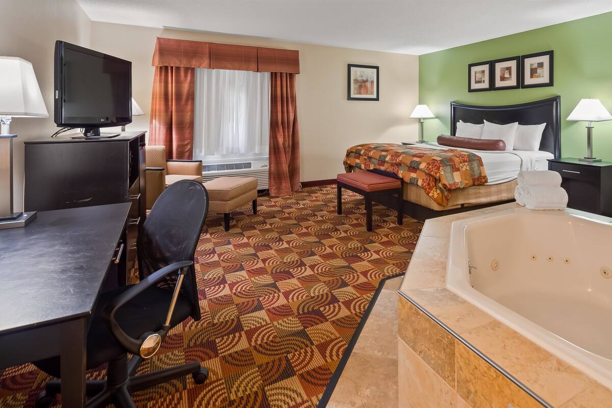 Hotelkamer met een groot bed, een bureau met een computer, een televisie, een badkamer met een bad en een kamerbreed tapijt met dessin.