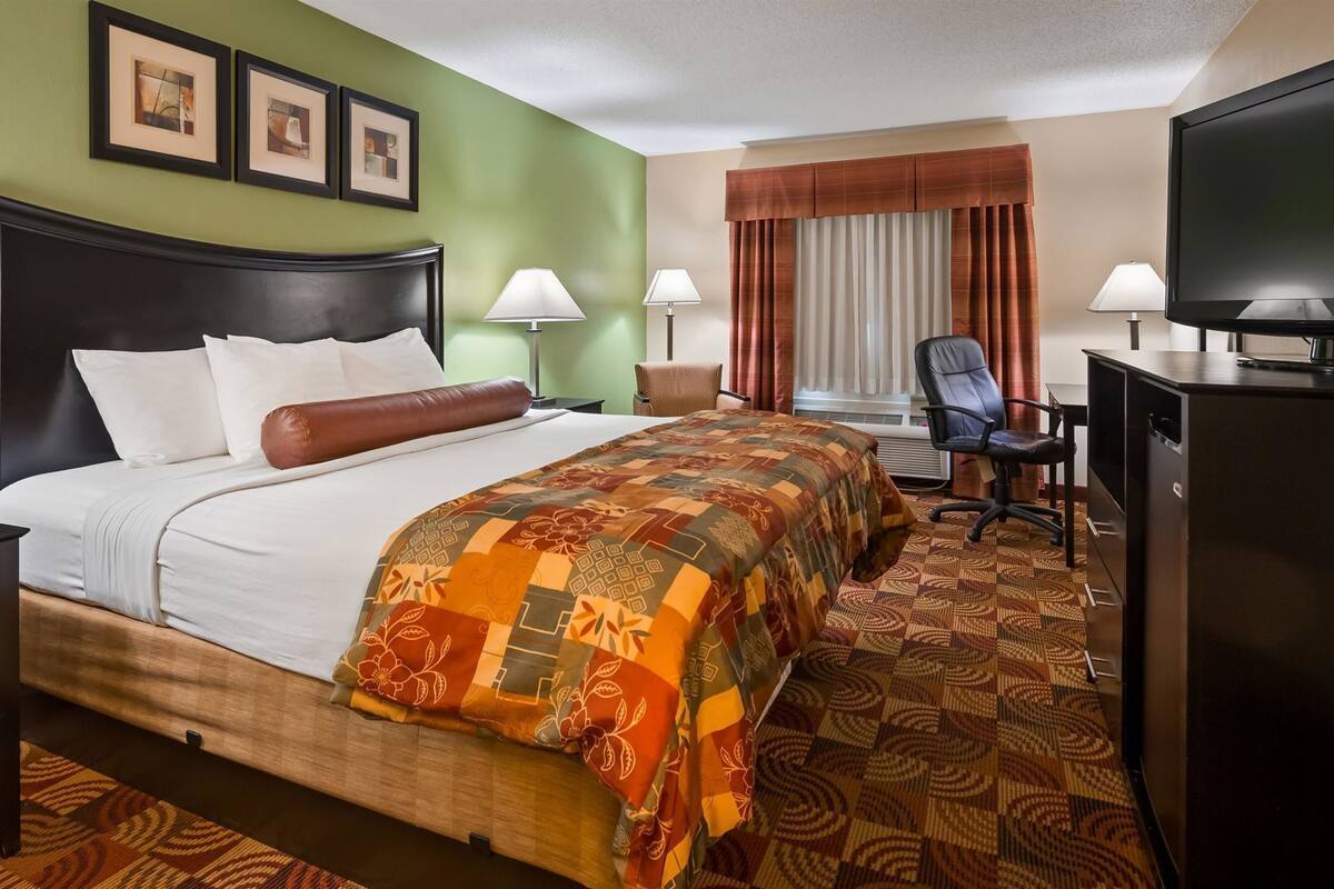 Hotelkamer met een bed, twee nachtkastjes, een bureau met stoel, een televisie en een raam met gordijnen.