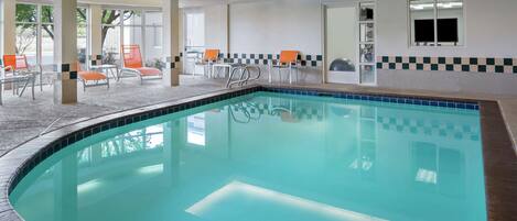 An indoor swimming pool with clear water, surrounded by lounge chairs and a tiled floor.