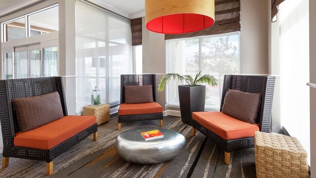 A modern lounge area with wicker chairs and orange cushions, a round metal coffee table, and a large potted plant. - Hilton Garden Inn Albuquerque North/Rio Rancho (Rio Rancho)