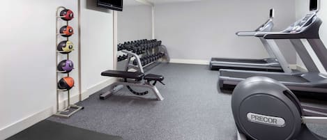Ett gym med löpband, en bänk, ett knäböjsställ och en TV som är monterad på väggen.