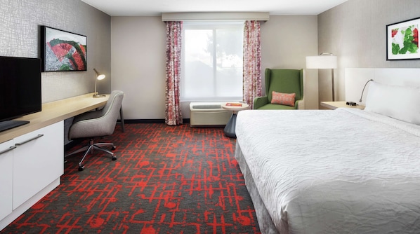 A hotel room with a bed, desk, chair, TV, and a window with curtains.