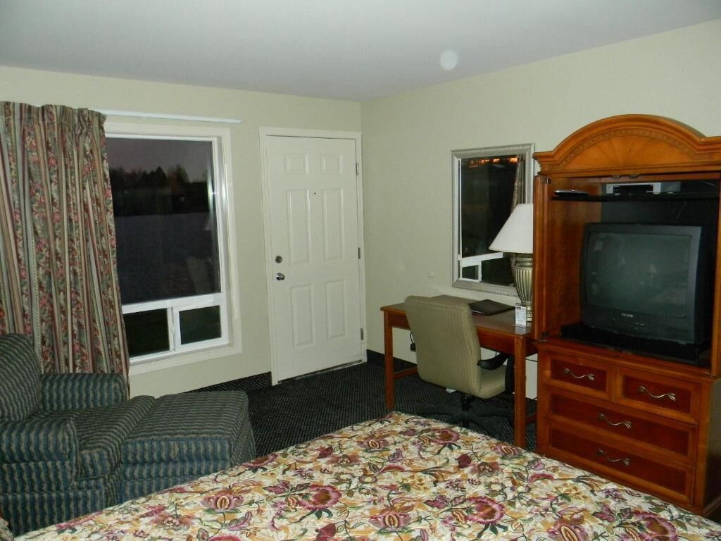 Habitación de hotel con cama, escritorio con computadora, televisión, silla y ventana con cortinas.