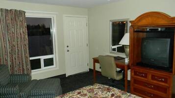 Habitación de hotel con cama, escritorio con computadora, televisión, silla y ventana con cortinas.