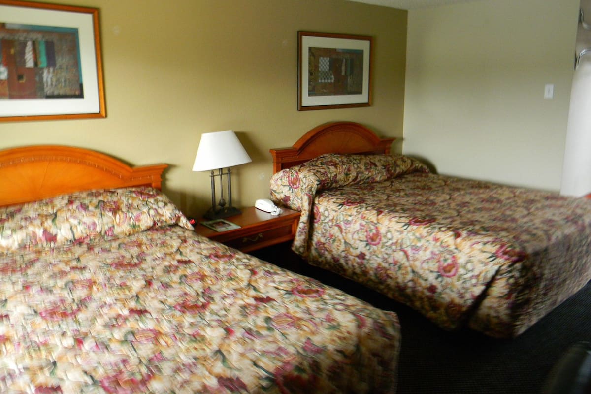 A hotel room with two single beds, a nightstand with a lamp, a phone, and framed artwork on the wall.