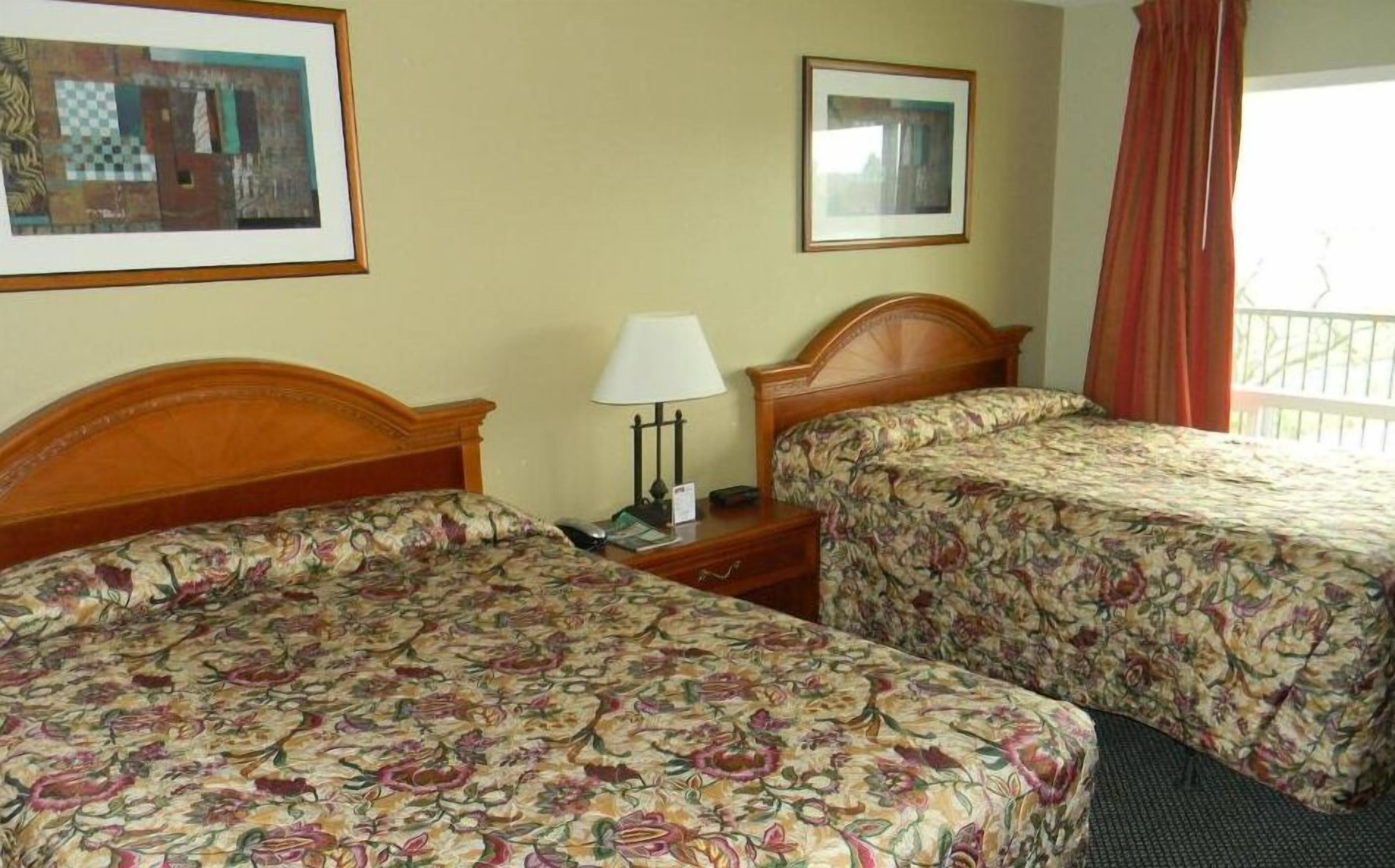 A hotel room with two beds, a nightstand, a lamp, and two framed pictures on the wall.