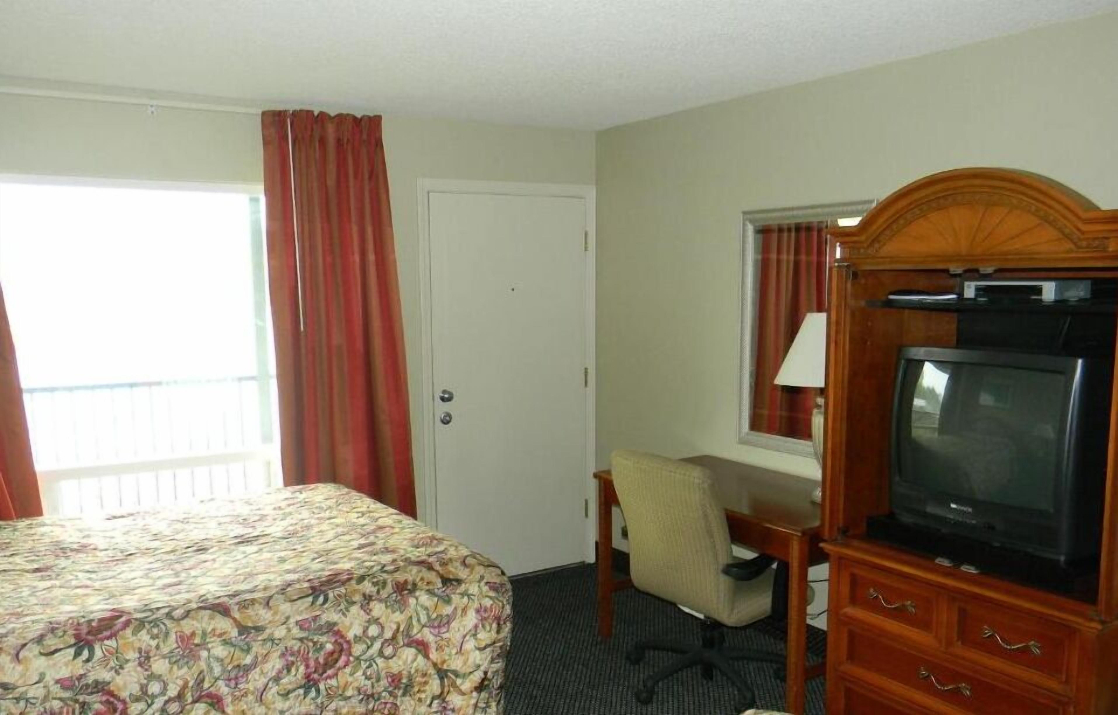 Une chambre d’hôtel comprenant un lit, un bureau avec une chaise, une télévision et une fenêtre avec des rideaux.