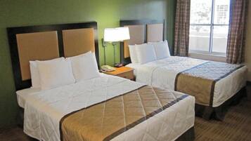 Two beds with headboards, a bedside lamp, and a window with curtains.